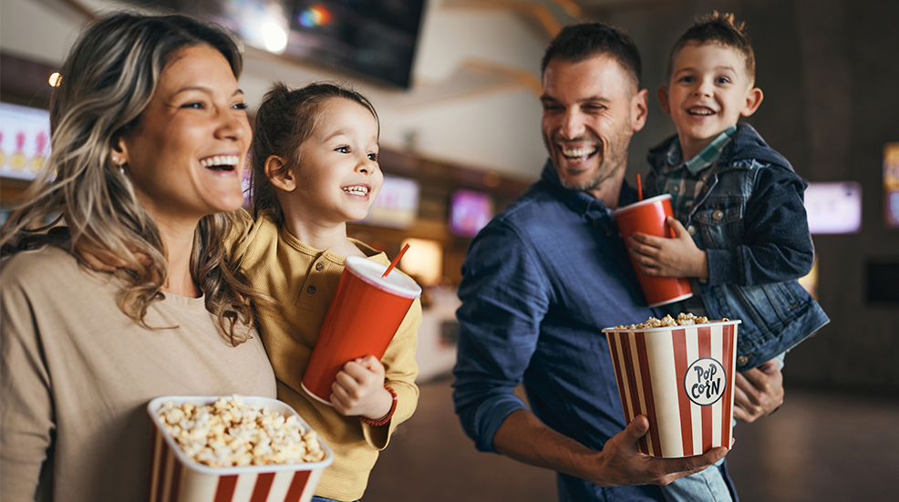 Young happy family with popcorn and drinks in movie theatre